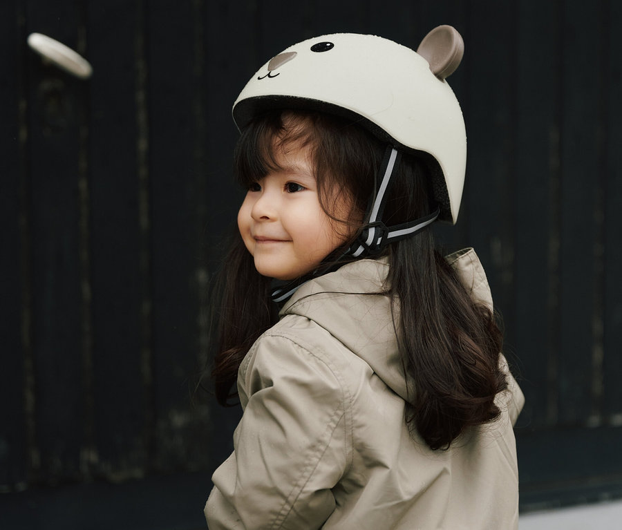 Lächelndes Mädchen mit braunen Haaren und Jacke fährt auf einem lila Laufrad. Sie trägt einen HUDORA Kinderhelm, Beary, 44–47 cm.