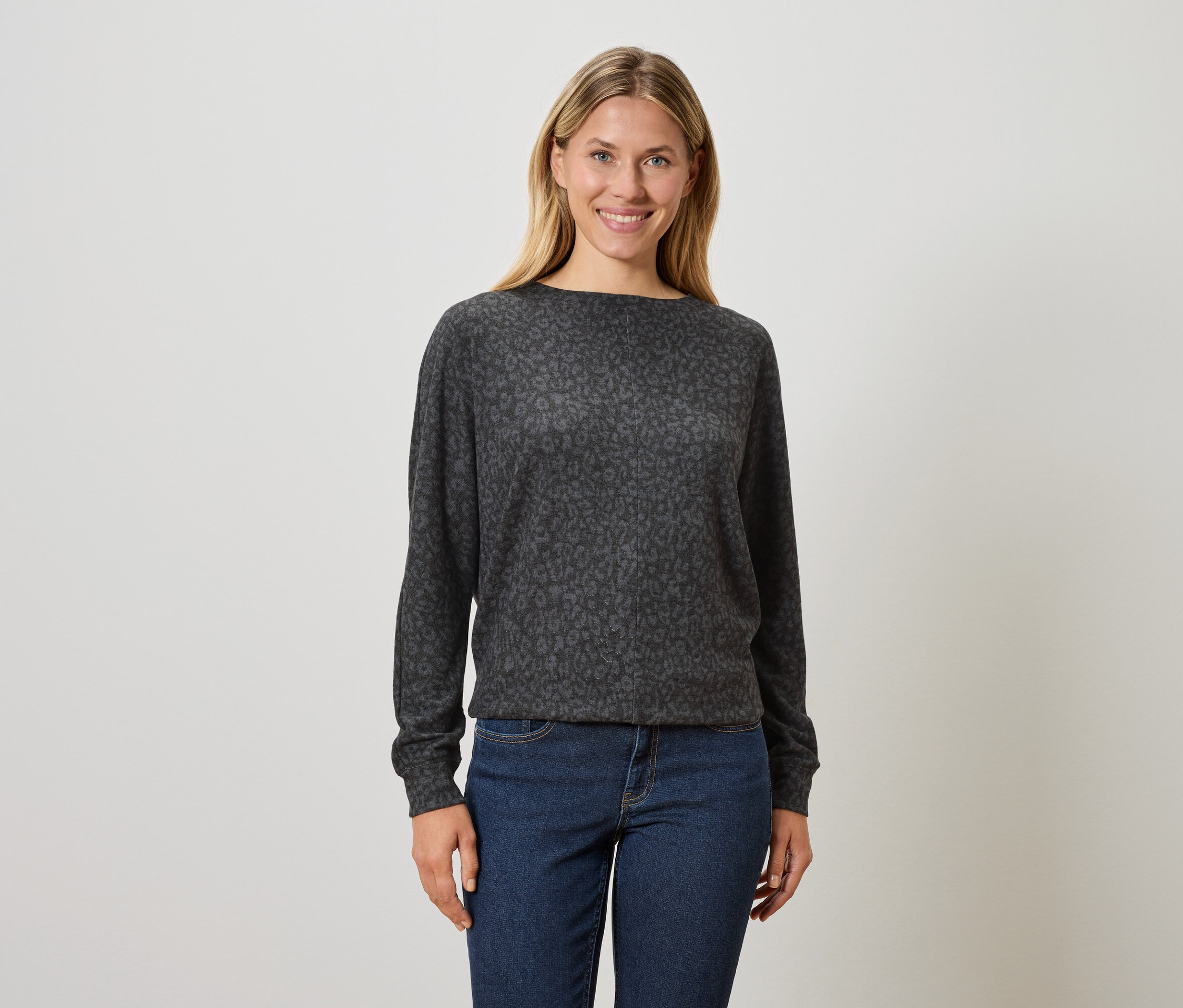 Frau mit blonden Haaren trägt einen dunkelgrauen Pullover mit Tiermuster und blaue Jeans.