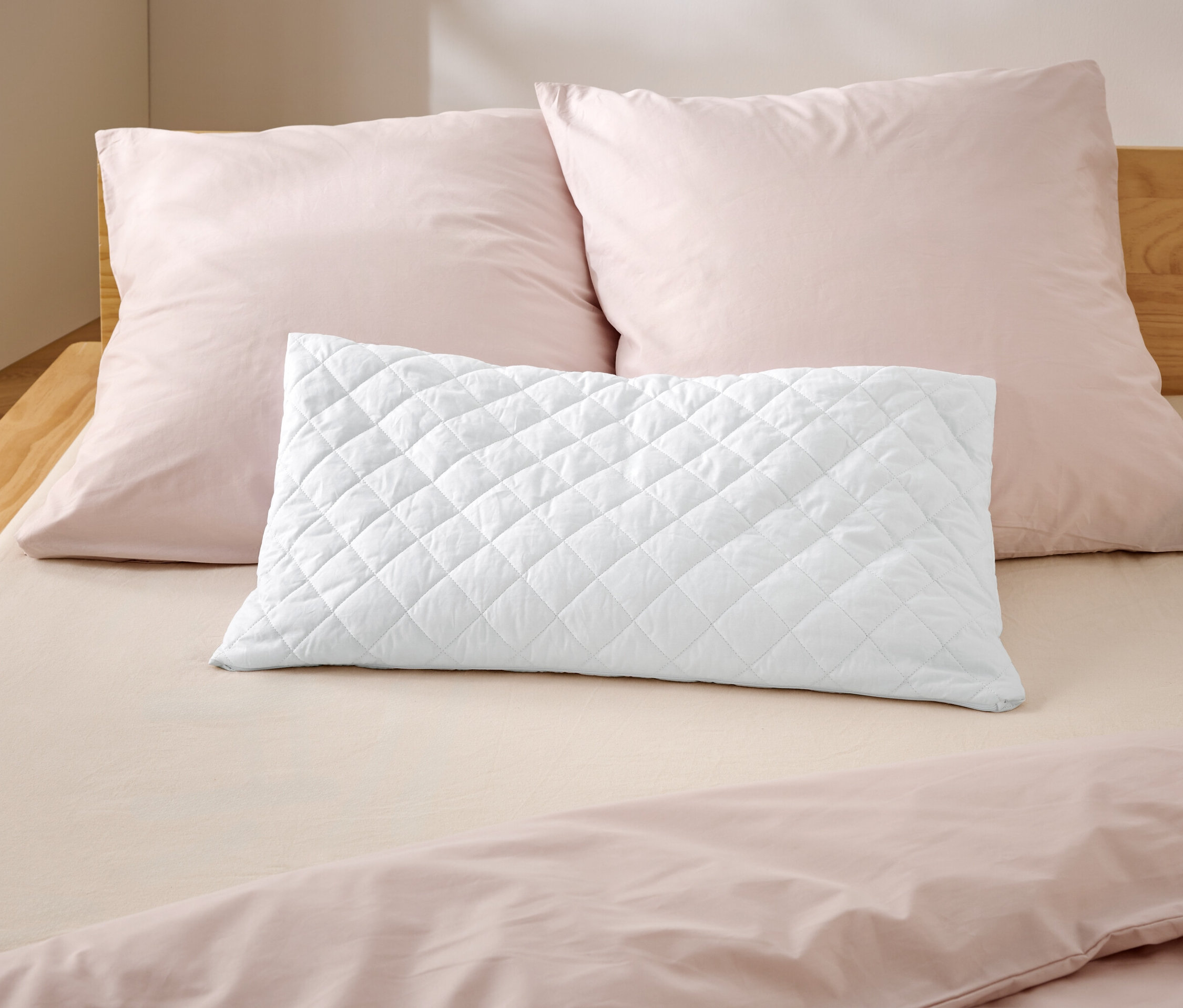 Auf einem Bett liegen zwei rosa Kissen und ein weißes, gestepptes Kissen.