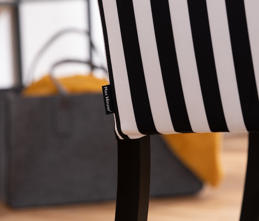 Nahaufnahme eines »Hendrick« Hochlehner-Polsterstuhls mit schwarz-weiß gestreiftem Bezug. Im Hintergrund eine graue Tasche mit gelben Textilien.
