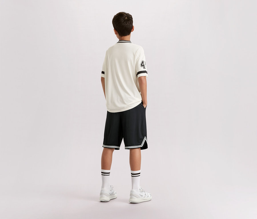 Ein Jugendlicher steht mit dem Rücken zur Kamera, er trägt ein helles T-Shirt mit der Nummer 4, schwarze Shorts, weiße Socken und Turnschuhe.