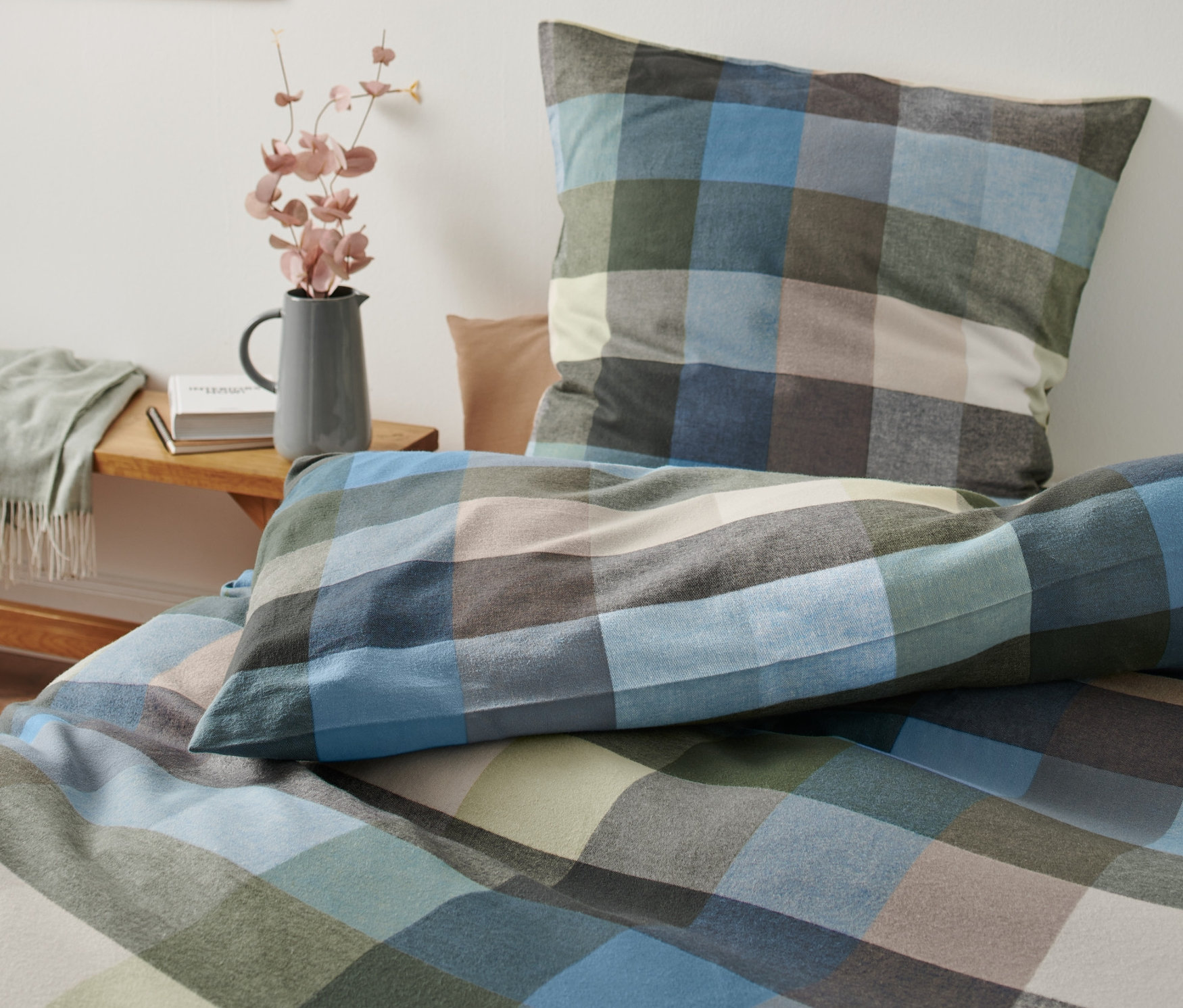 Karierte Flanell-Bettwäsche, Normalgröße, liegt auf einem Bett neben einer Vase mit Blumen.