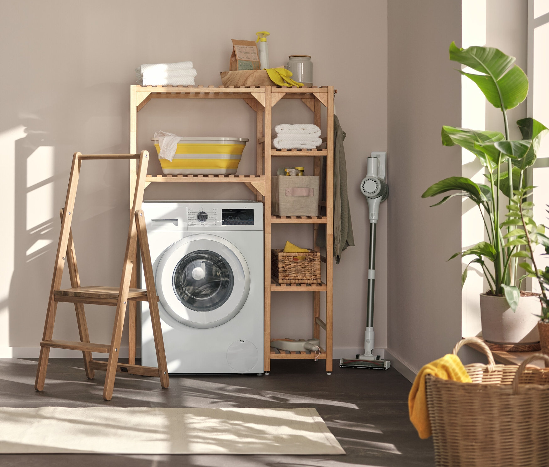Im Waschraum stehen eine Waschmaschine, darüber ein Waschmachinenregal mit Seitenelement, links davon ein Wandregal mit flexiblen Haken und Boden und eine Trittleiter aus Massivholz.