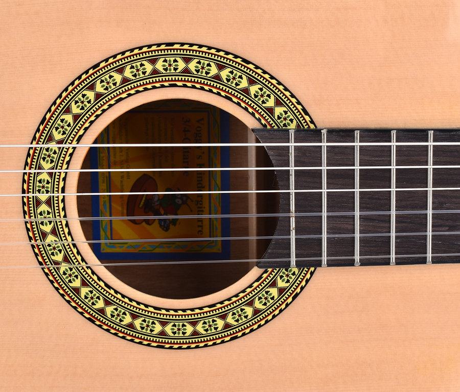 Detailaufnahme einer Voggenreiter Kindergitarren-Set, 3/4, ab 8 J. Akustikgitarre mit braunem Griffbrett und kreisförmigem Zierelement um das Schallloch.