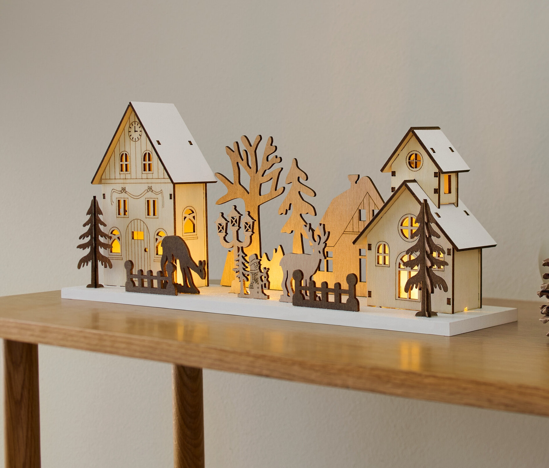Ein LED-Winterdorf aus Holz mit Häusern und Bäumen steht auf einem Tisch.