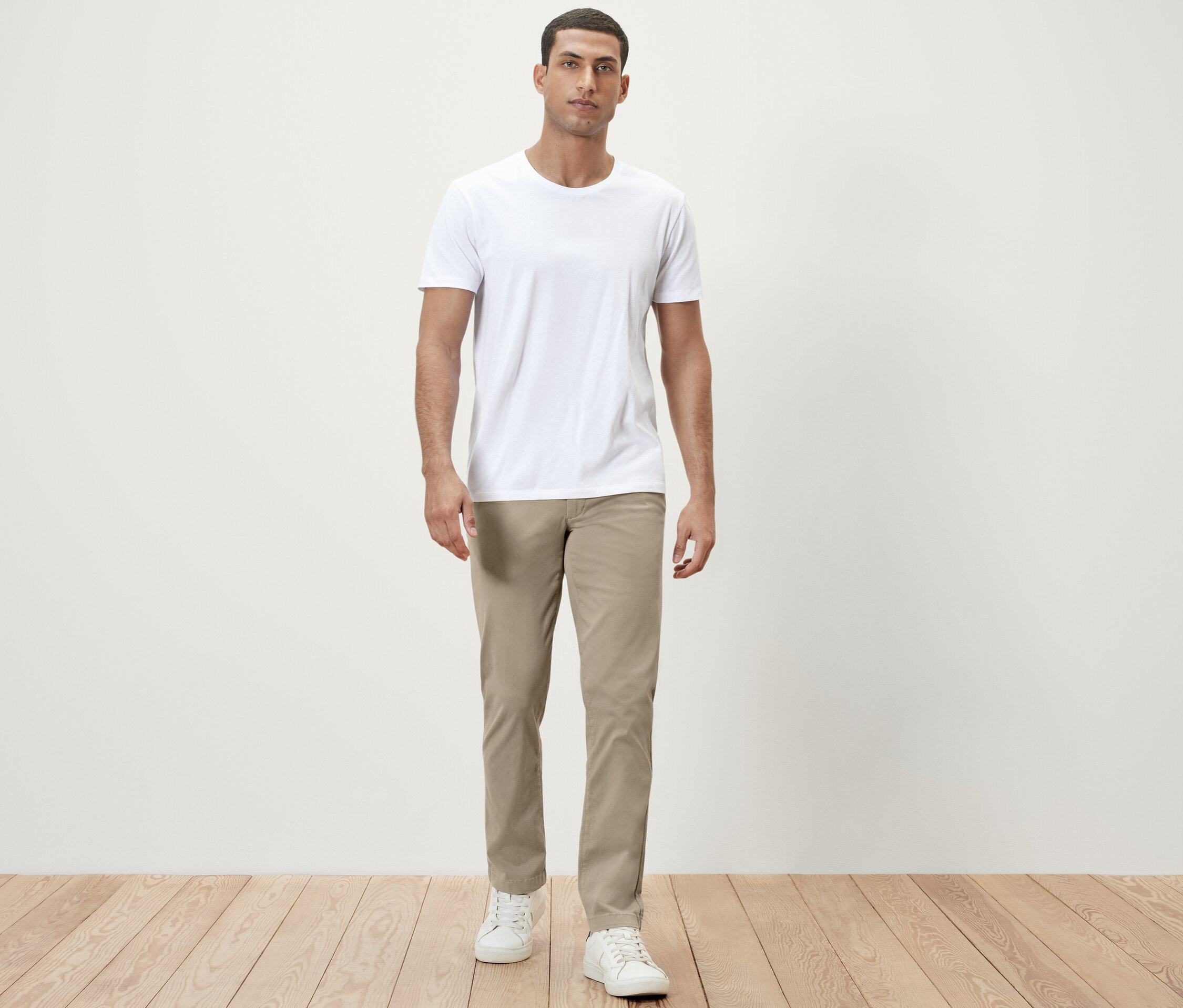 Mann steht in weißem T-Shirt und beiger Chino.