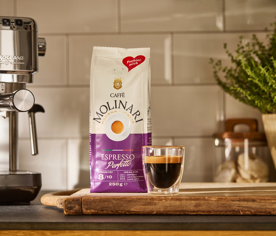 Eine silberne »Lapressa« Siebträgermaschine, eine Packung Caffè Molinari und eine Tasse Espresso auf einem Holzbrett.