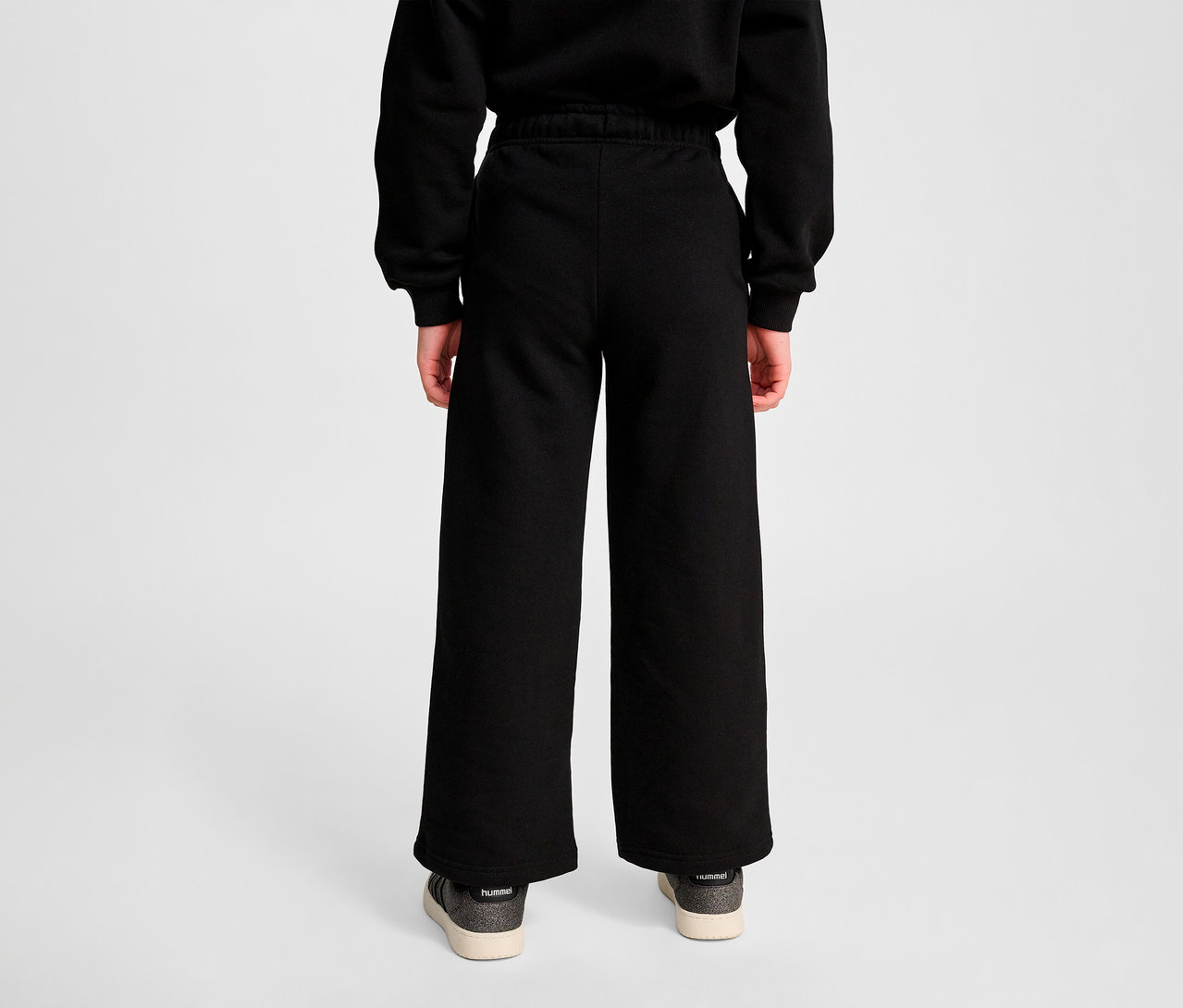 Person von hinten trägt schwarze HUMMEL HMLJR Loose WL Sweatpants und Schuhe.