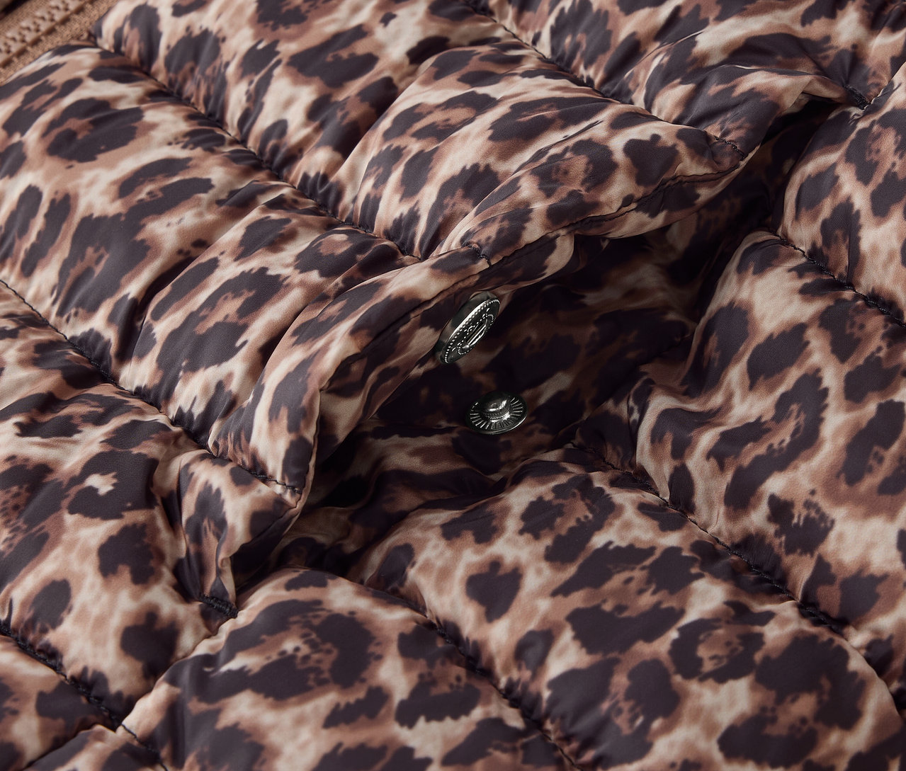 Detailaufnahme einer braunen Steppjacke mit Tiermuster und silbernen Druckknöpfen.