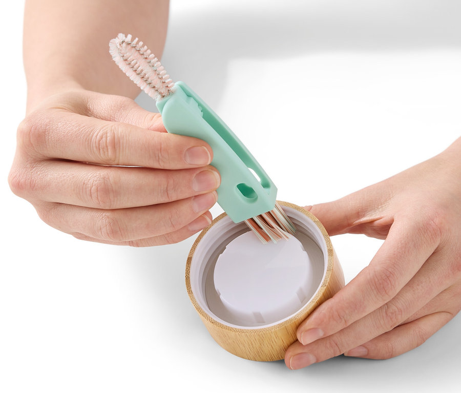 Hände reinigen einen Flaschendeckel mit einer 3-in-1-Reinigungsbürste.