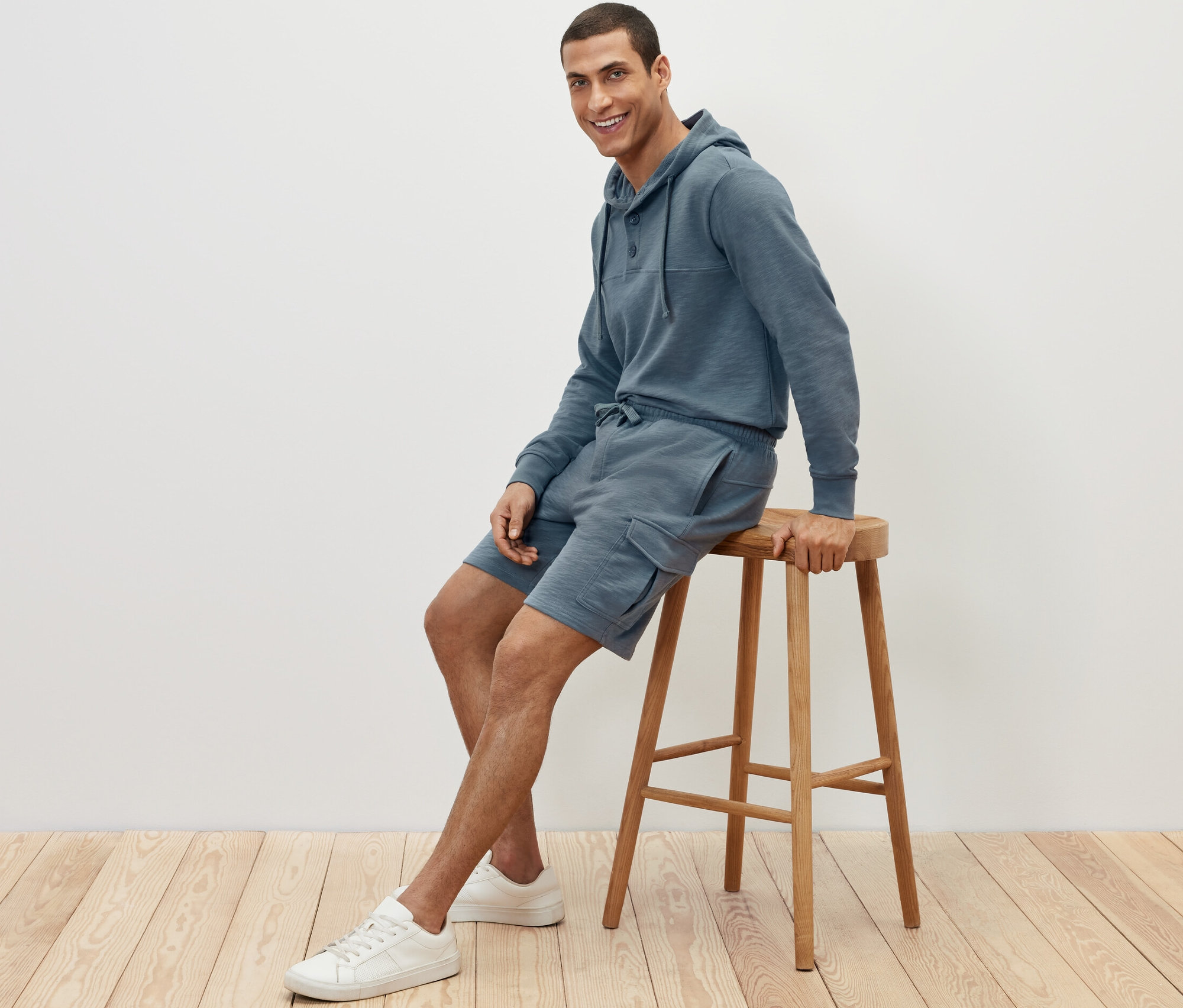 Ein Mann sitzt auf einem Hocker und trägt Cargo-Sweatshorts und einen Hoodie.