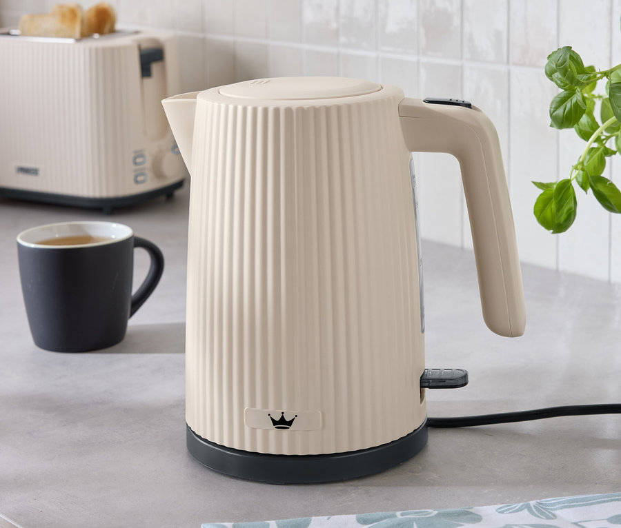 Auf einer Küchentheke stehen ein cremefarbener Wasserkocher, ein Toaster, eine Tasse und ein Küchentuch.