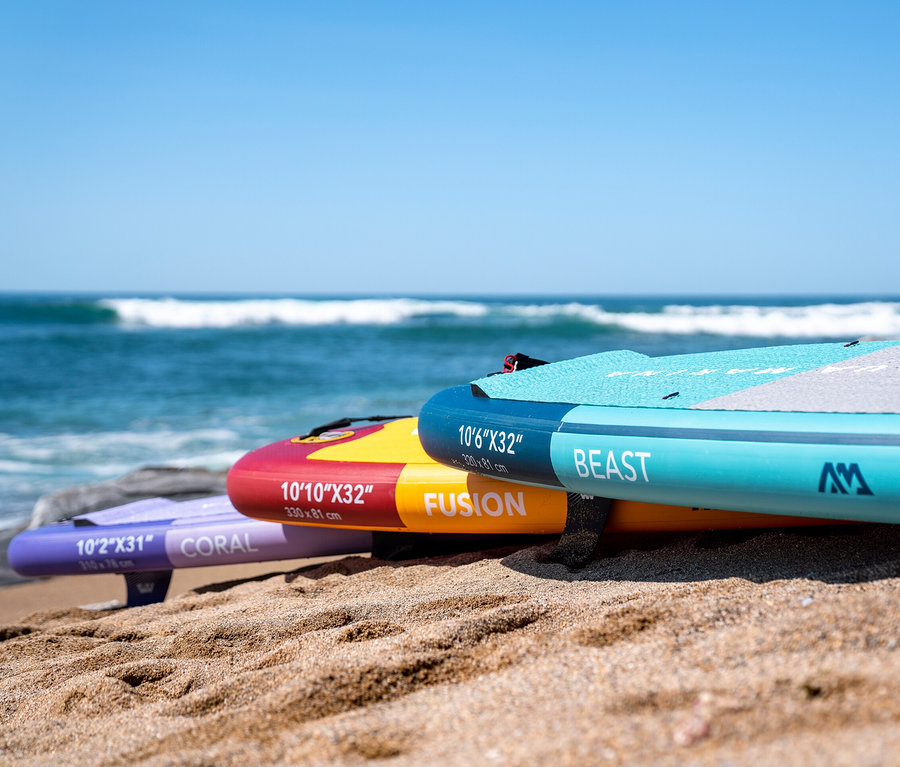 Drei Aqua Marina SUP-Boards liegen am Strand, im Hintergrund das Meer.