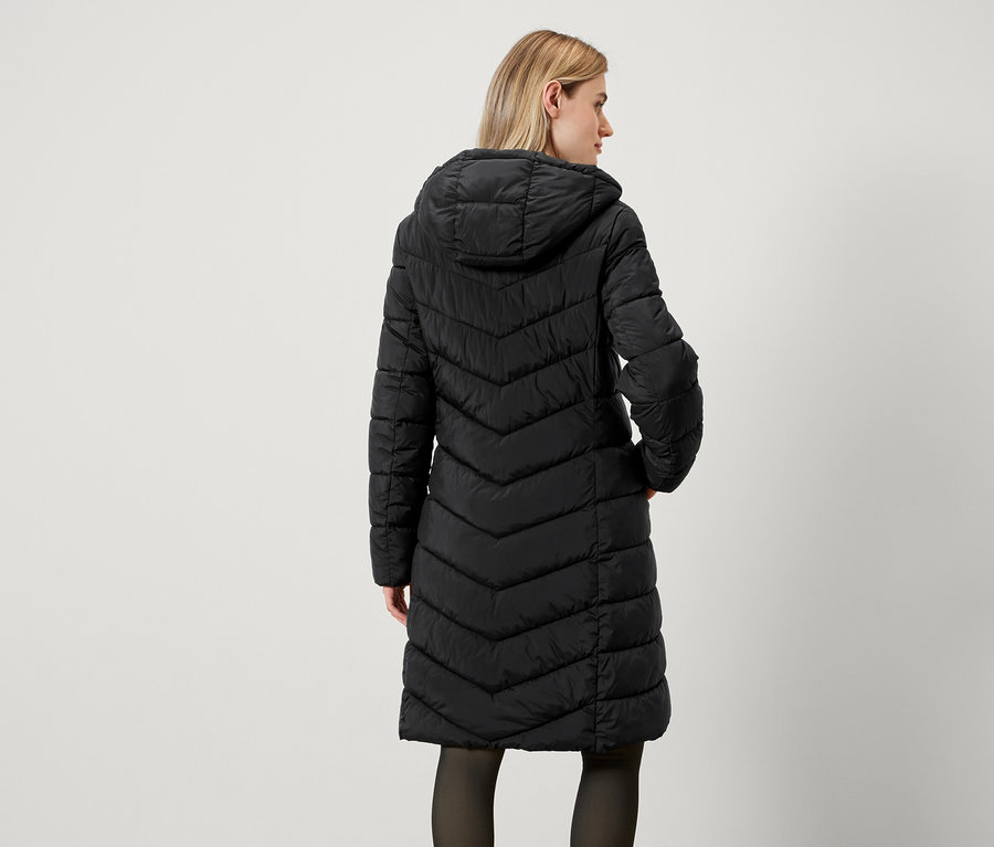 Rückansicht einer Frau in einem langen, schwarzen Steppmantel mit Kapuze.