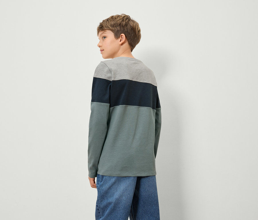 Ein Junge in einem farbigen Langarmshirt und Jeans steht mit dem Rücken zur Kamera.