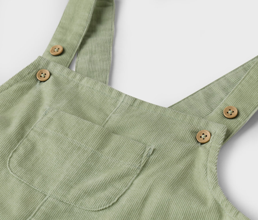 Nahaufnahme einer hellgrünen Cordhose mit Trägern, die mit Knöpfen befestigt sind und einer aufgesetzten Tasche.