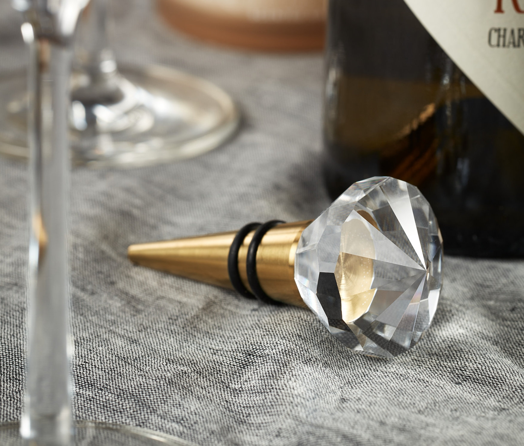 Auf einem grauen Tuch liegen zwei Flaschenkorken neben einem Weinglas und einer Weinflasche.