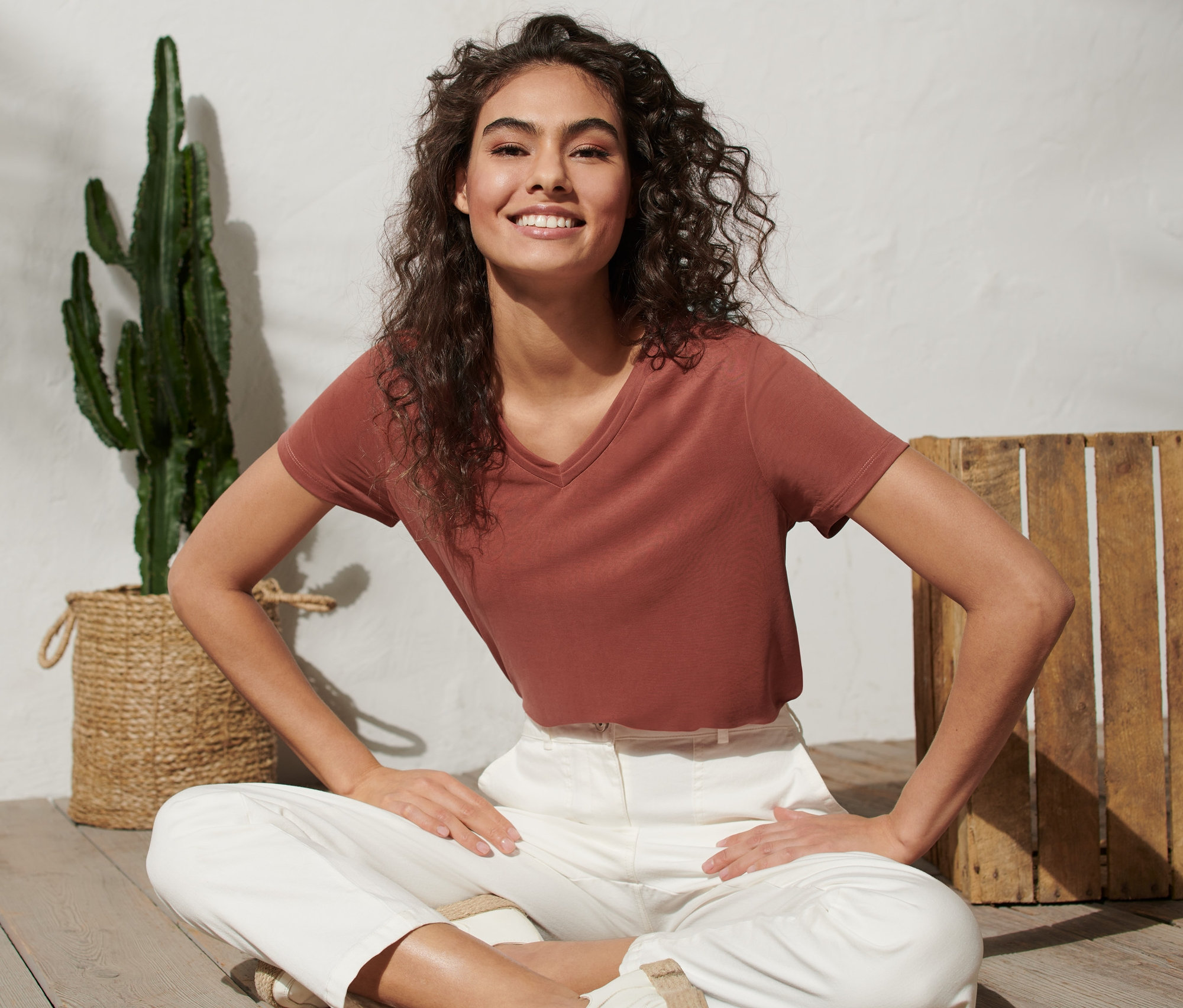 Eine Frau sitzt mit gekreuzten Beinen auf dem Boden und trägt ein T-Shirt.