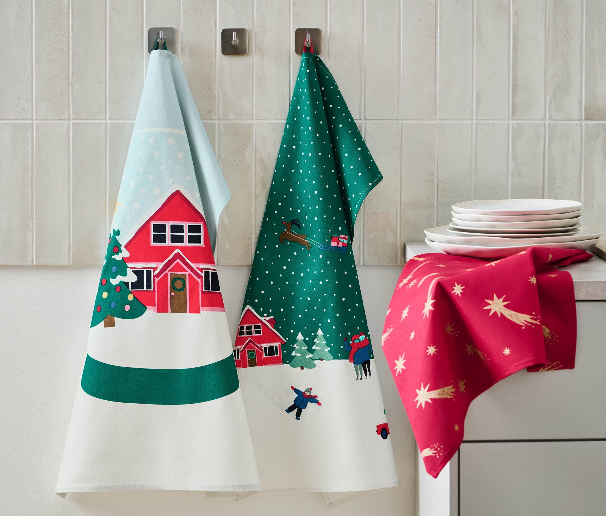 Drei Geschirrtücher mit Weihnachtsmotiven hängen an der Wand. Auf der Arbeitsfläche liegen Teller und ein Seifenspender.