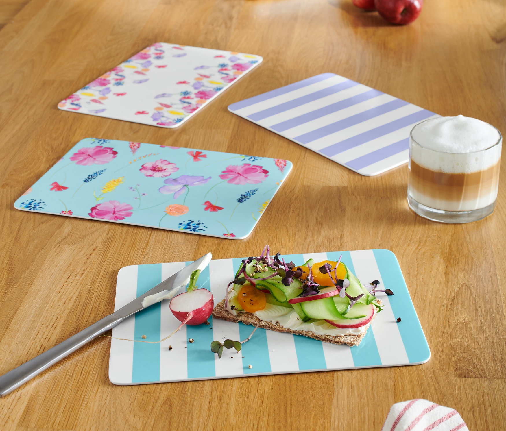 Vier Schneidebretter liegen auf einem Holztisch. Auf einem liegt ein Messer und Brot mit Gemüse.