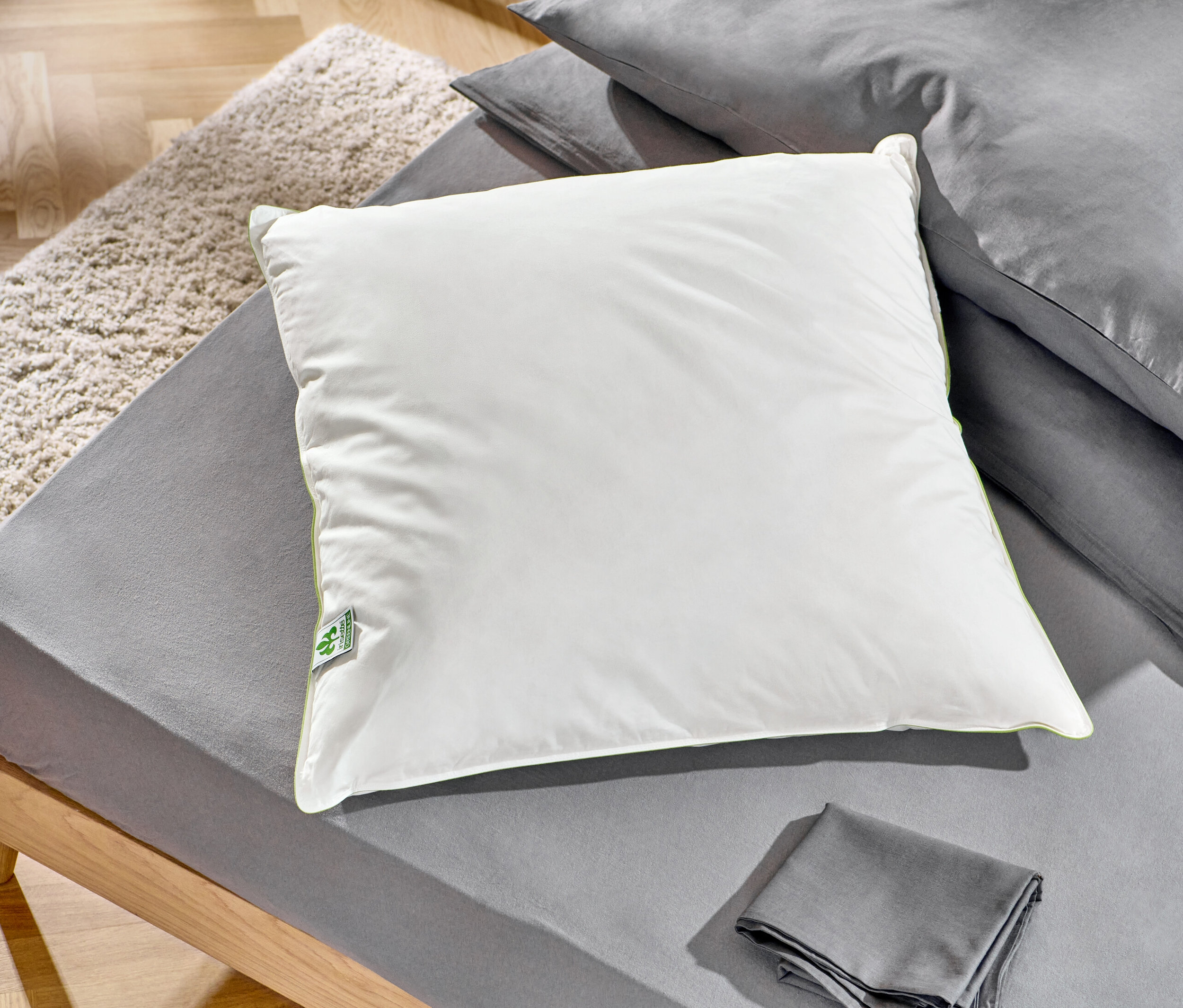 Auf einem Bett liegen zwei irisette® greenline Federkopfkissen, ca. 90 x 70 cm und ca. 80 x 80 cm.