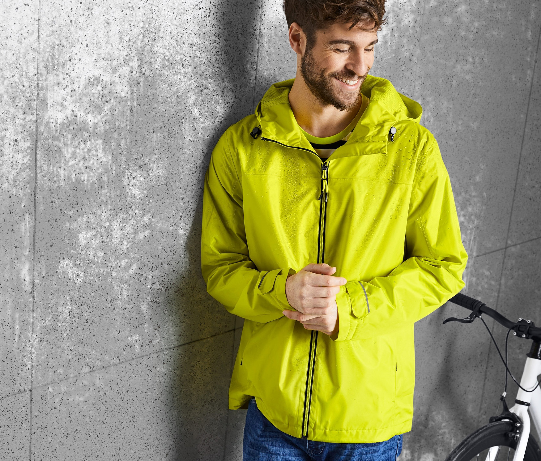 Mann lehnt an Wand, trägt gelbe Regenjacke.