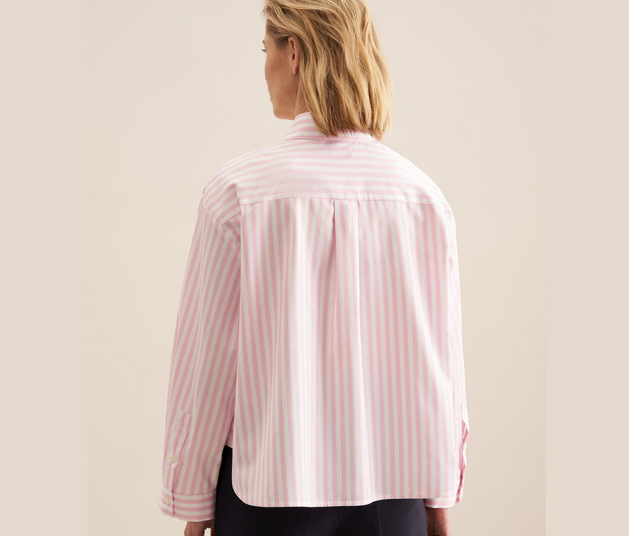 Frau trägt eine rosafarbene Seidensticker Oversize Hemdbluse mit weißen Streifen.
