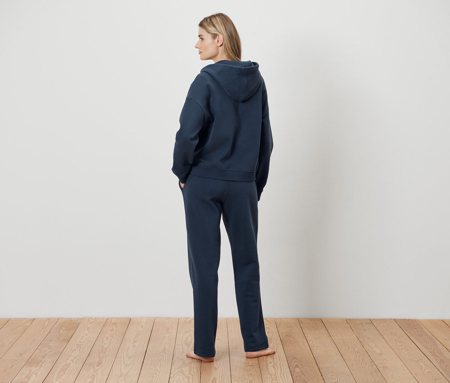 Frau steht mit dem Rücken zur Kamera und trägt einen dunkelblauen Hoodie und eine Jogginghose.