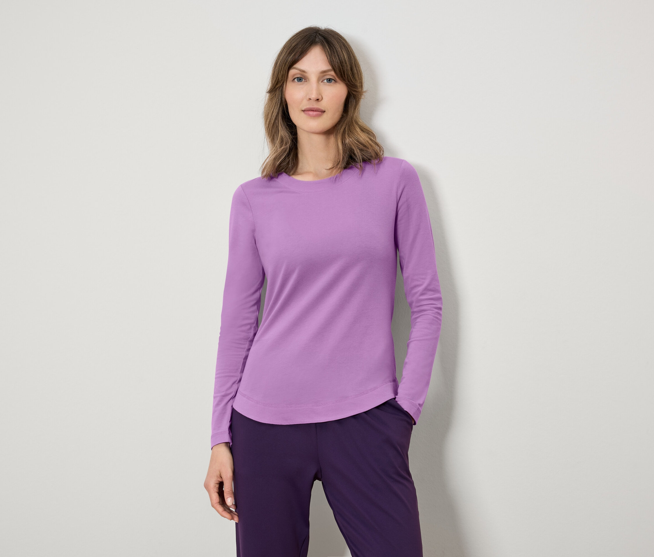 Frau trägt ein lila langärmeliges Hemd und dunkelviolette Hosen.