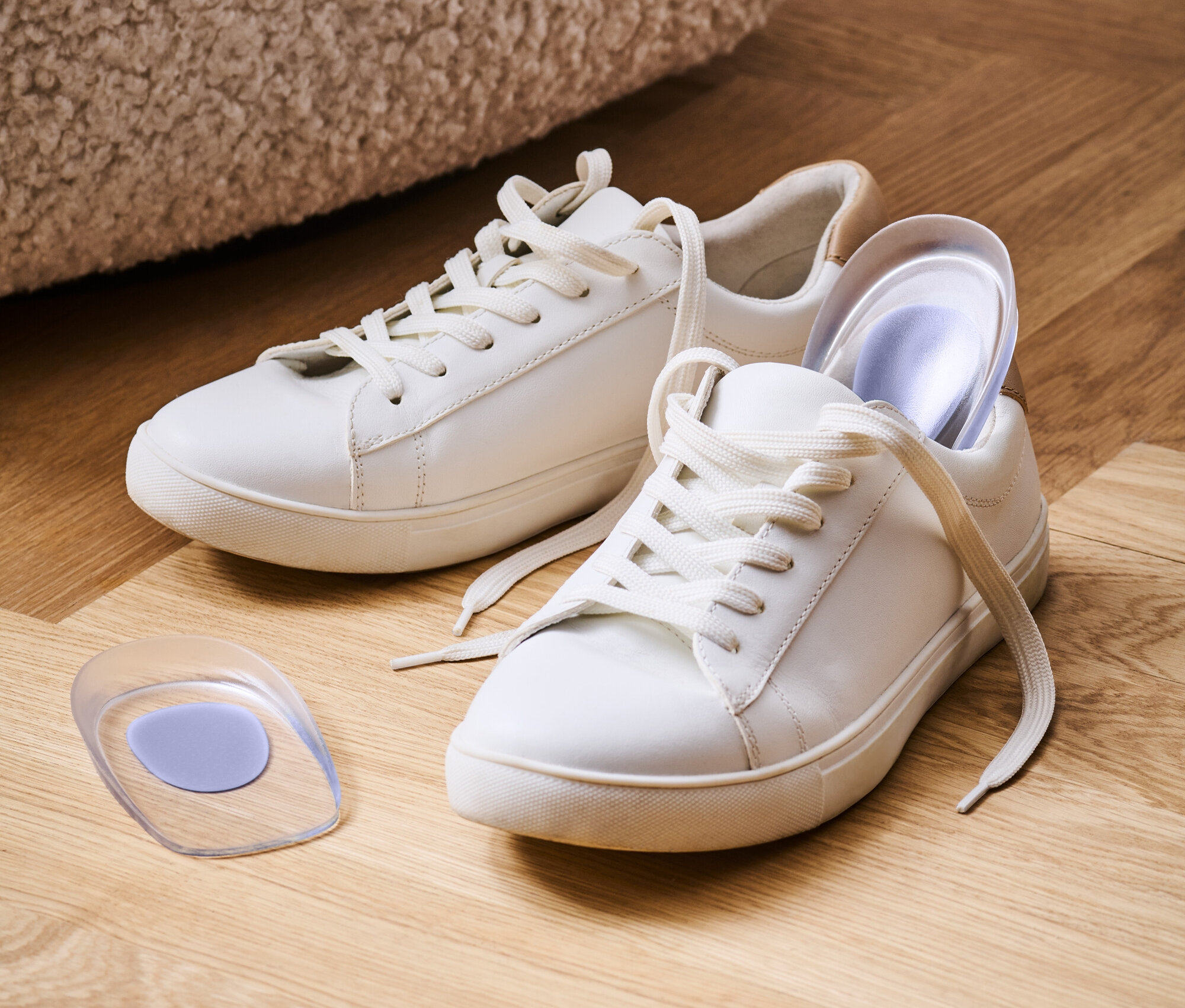 Zwei weiße Turnschuhe mit weißen Schnürsenkeln auf einem Holzboden mit einer Gelsohle.