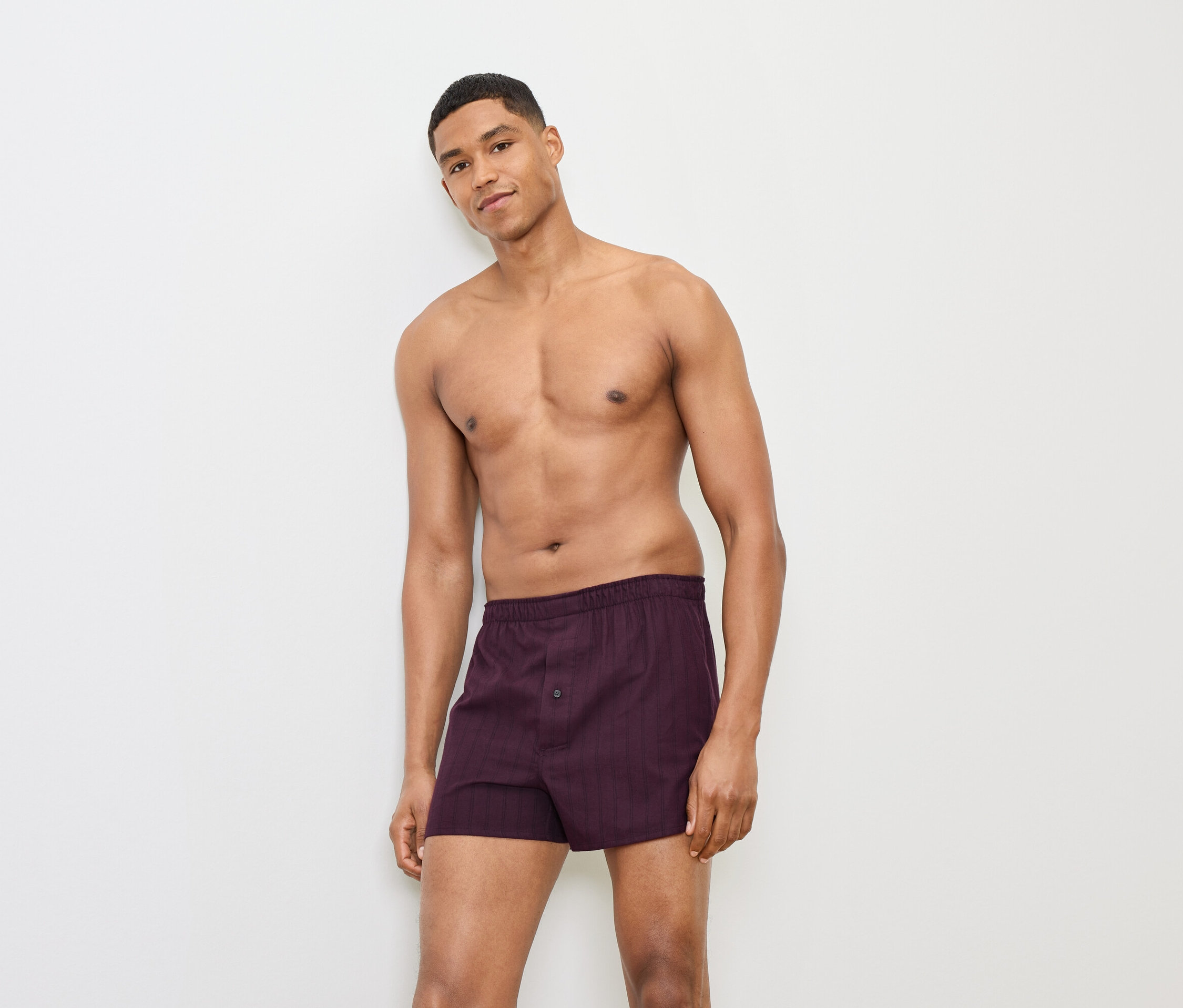 Mann posiert in burgunderfarbener Boxershorts vor einem weißen Hintergrund.