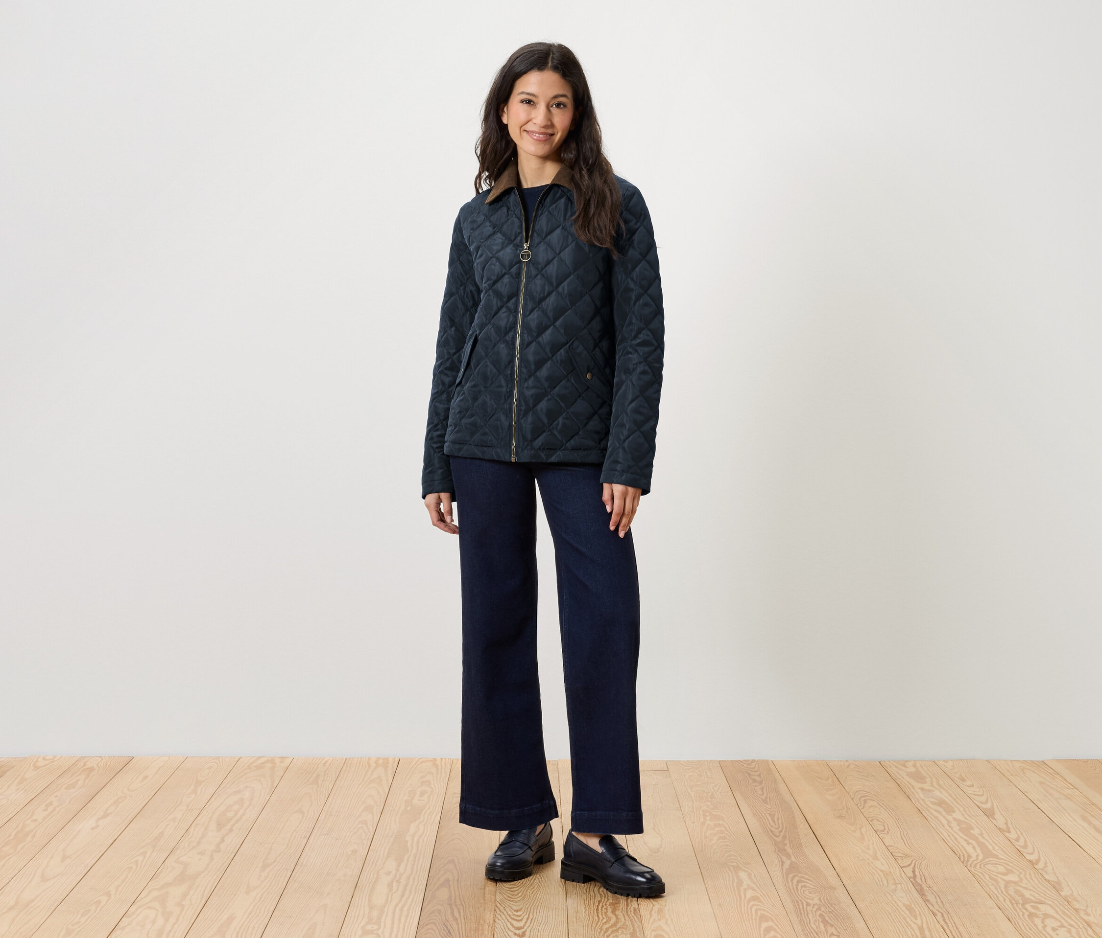 Frau steht und trägt eine gesteppte Jacke, Jeans und Slipper.