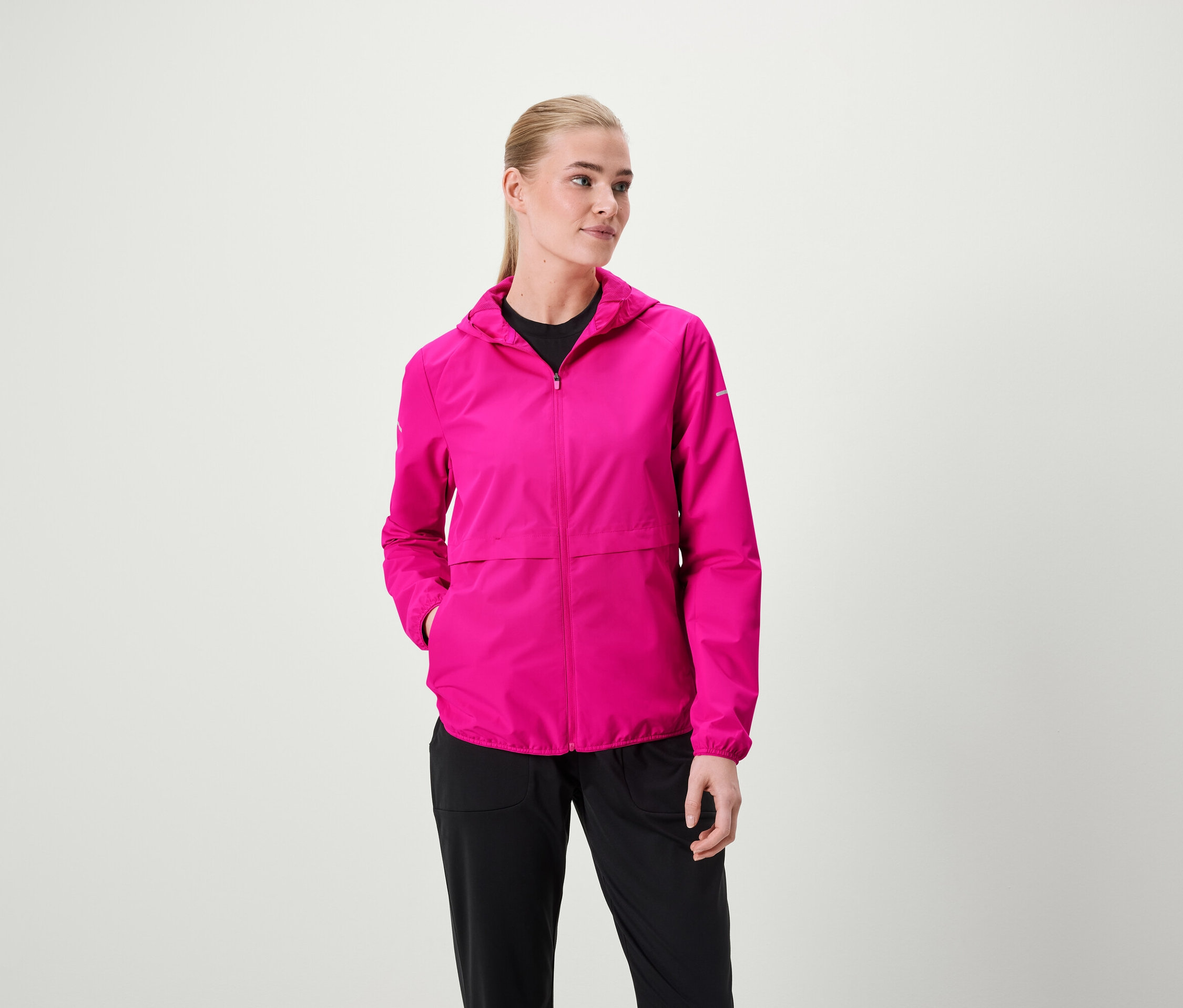 Frau trägt eine pinke Kapuzenjacke und schwarze Hosen.