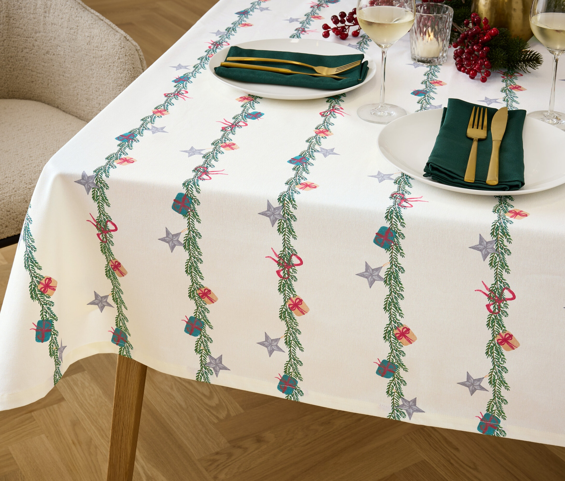 Detailaufnahme eines Tisches mit einer weihnachtlichen Tischdecke, Tellern, Besteck und Gläsern.