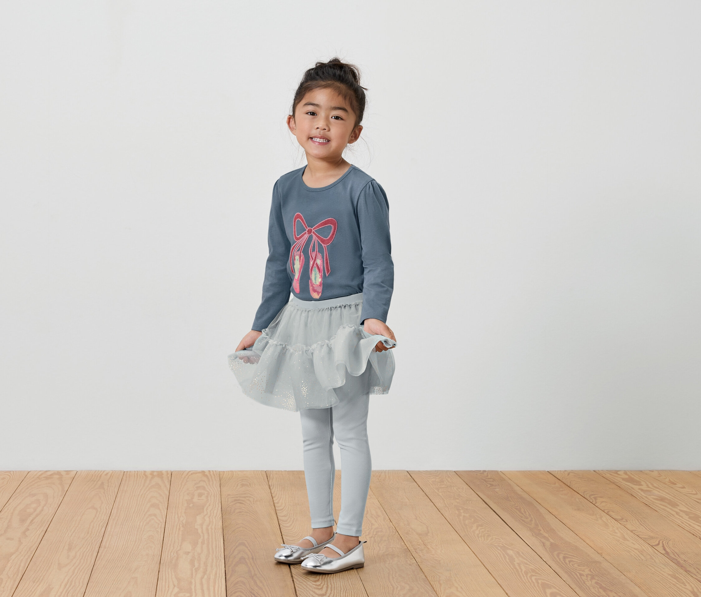 Mädchen im grauen Ballett-Outfit mit T-Shirt, Rock und Leggings.