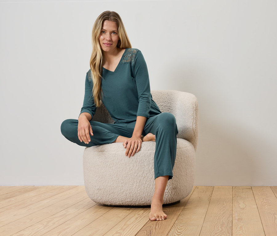Frau sitzt in grüner Pyjamahose und Oberteil auf einem Sessel.