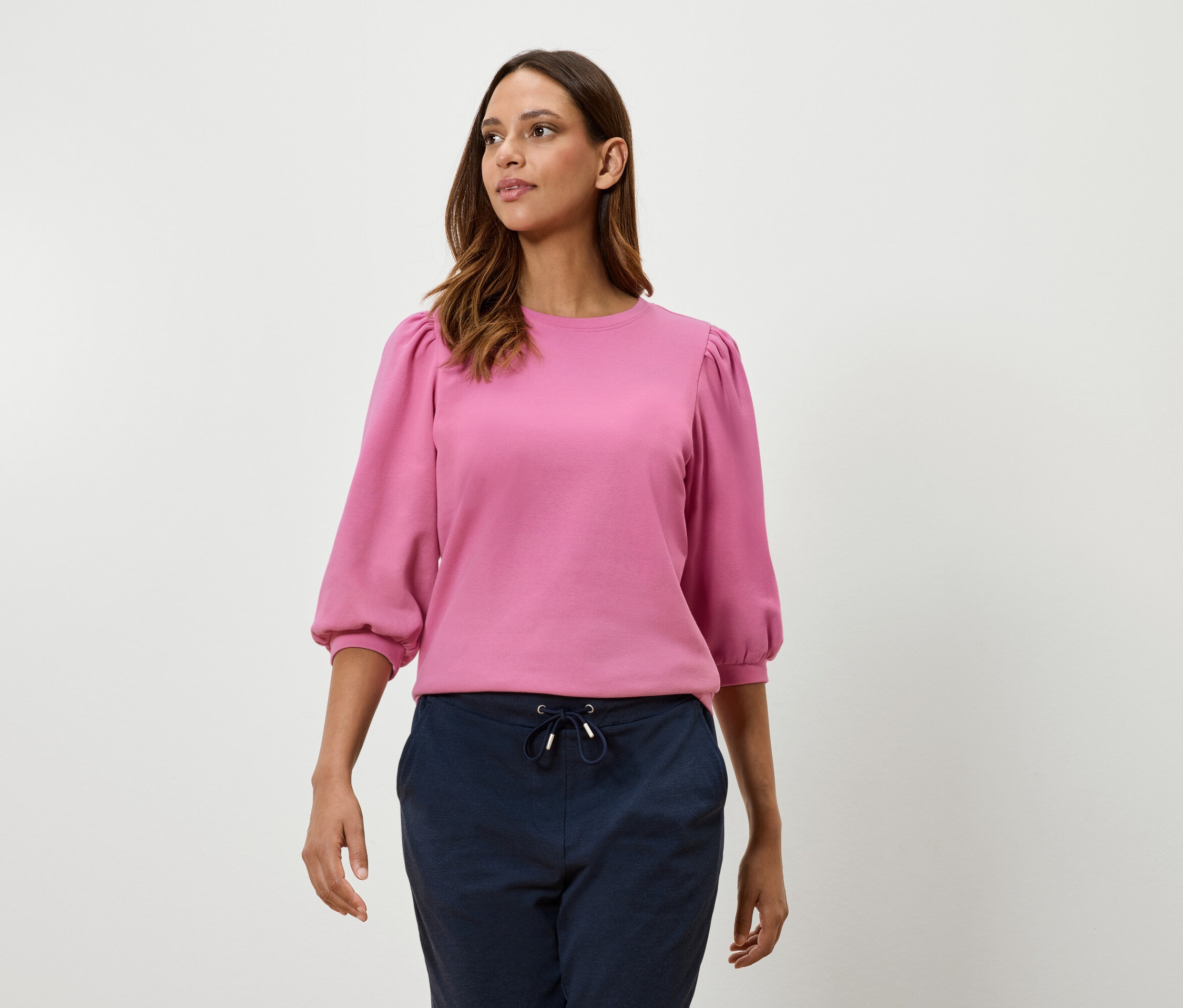 Frau trägt ein pinkes Sweatshirt mit Dreiviertel-Ballonärmeln und marineblaue Hosen.