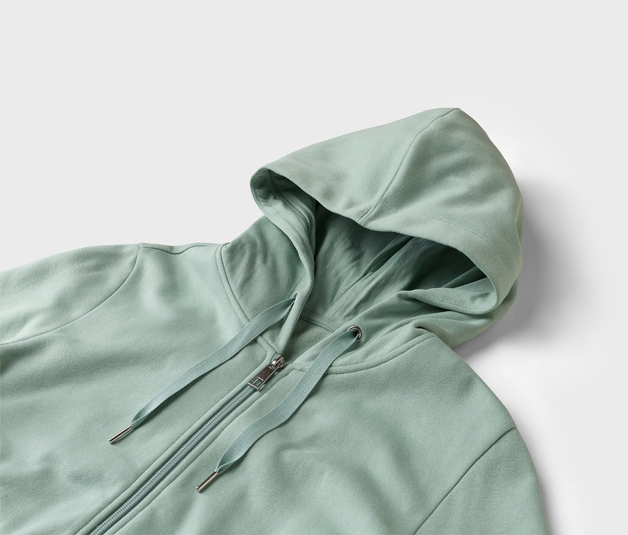 Nahaufnahme eines hellgrünen Kapuzenpullovers mit Reißverschluss auf weißem Hintergrund.