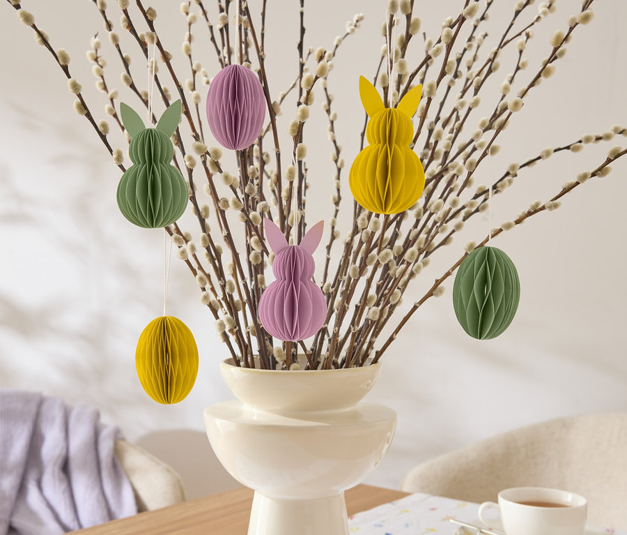 Dekorative Osterzweige mit hängenden Papierornamenten in Hasen- und Eiform in Gelb, Grün und Lila in einer Vase.
