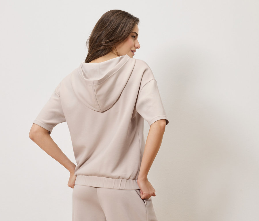 Frau von hinten, die einen beigen Kapuzenpullover und eine passende Hose trägt.