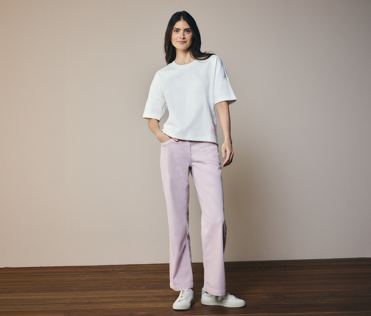 Frau in weißem Shirt und CECIL Jeans »Neele«. Sie steht auf Holzboden vor beigem Hintergrund.