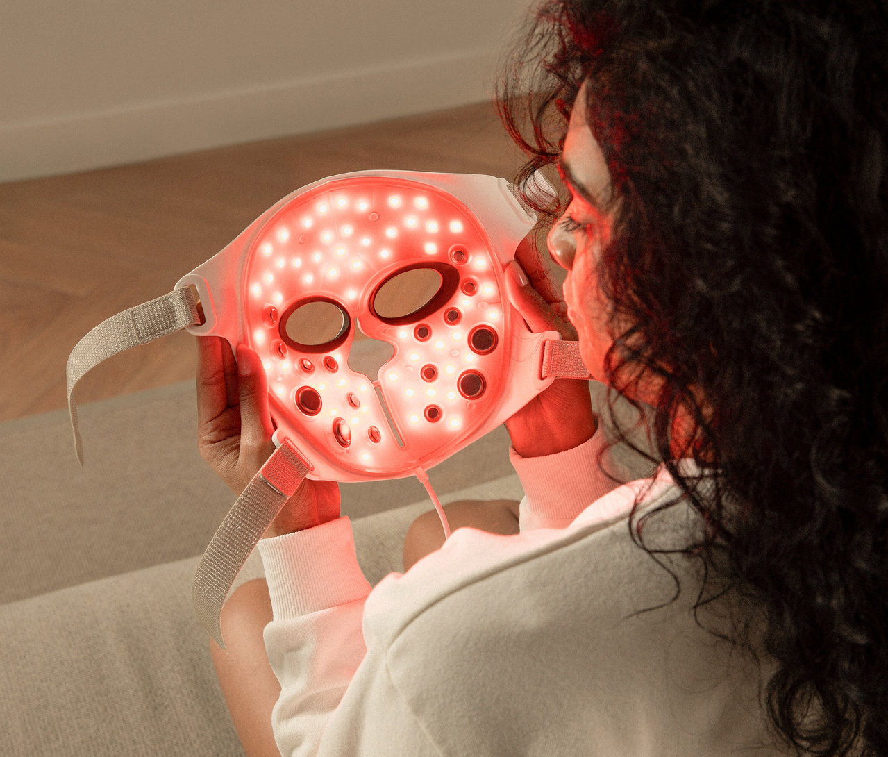 Frau hält Silk'n LED Gesichtsmaske mit EMS vor ihr Gesicht.