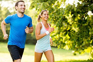 Sport an warmen Tagen: Ein junger Mann und eine junge Frau, die beide Sportshorts tragen, joggen an einem warmen Sommertag nebeneinander her.