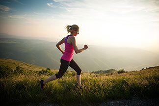 Eine junge, blonde Frau, die eine 3/4-Sporthose trägt, joggt über eine Wiese.