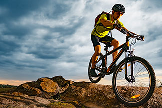 Ein junger Mann, der als Fahrradbekleidung ein kurzärmliges Fahrradtrikot und eine kurze Radlerhose trägt, fährt auf einem Mountainbike in den Bergen.