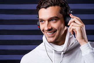 Ein junger Mann in einem hellen, modernen Rollkragenpullover hört Musik über kabelgebundene Kopfhörer.