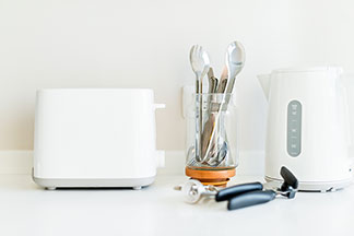 Hilfreiche Küchengeräte: Eine Arbeitsplatte auf der ein Wasserkocher, ein Toaster, Besteck in einem Glas, ein Korkenzieher sowie ein Dosenöffner liegen.