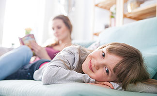 Wohlfühlen durch gute Qualität: Ein Kind liegt lächelnd auf dem Sofa, während seine Mutter aus einem Buch vorliest.