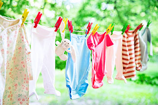 Eine Wäscheleine hängt im Freien – an ihr befindet sich Babykleidung, die mit roten, gelben und grünen Wäscheklammern befestigt ist.