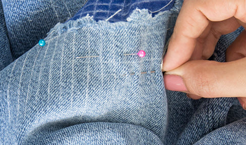 Stecknadeln werden in eine Jeans gesteckt